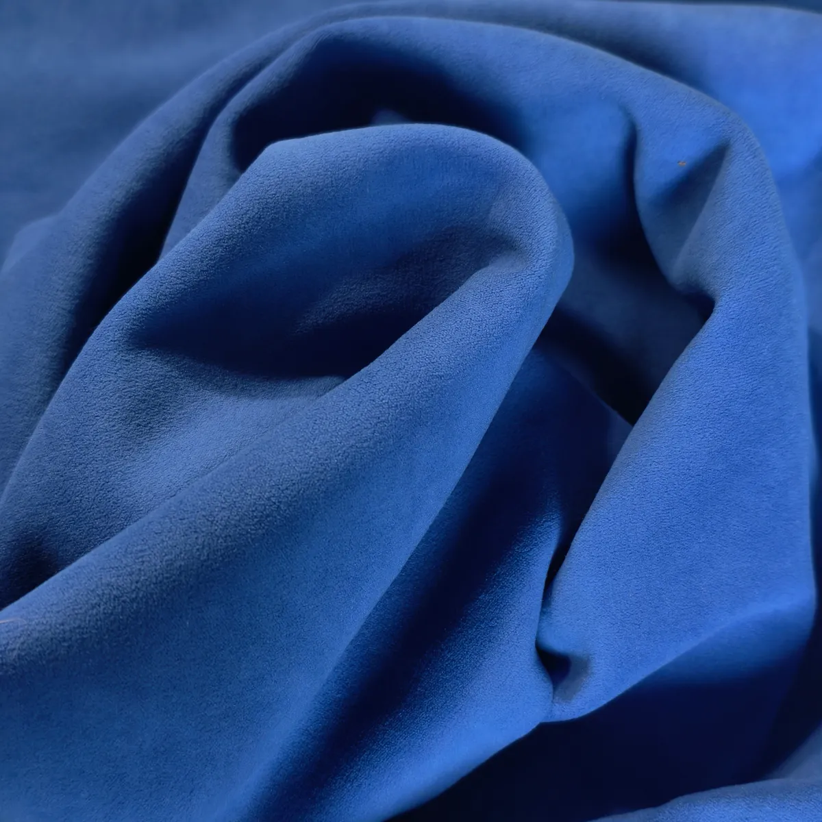 Nærbillede af blåt Brazio-tekstil arrangeret i bløde bølger, som fremhæver stoffets matte finish og glatte, rolige overflade.